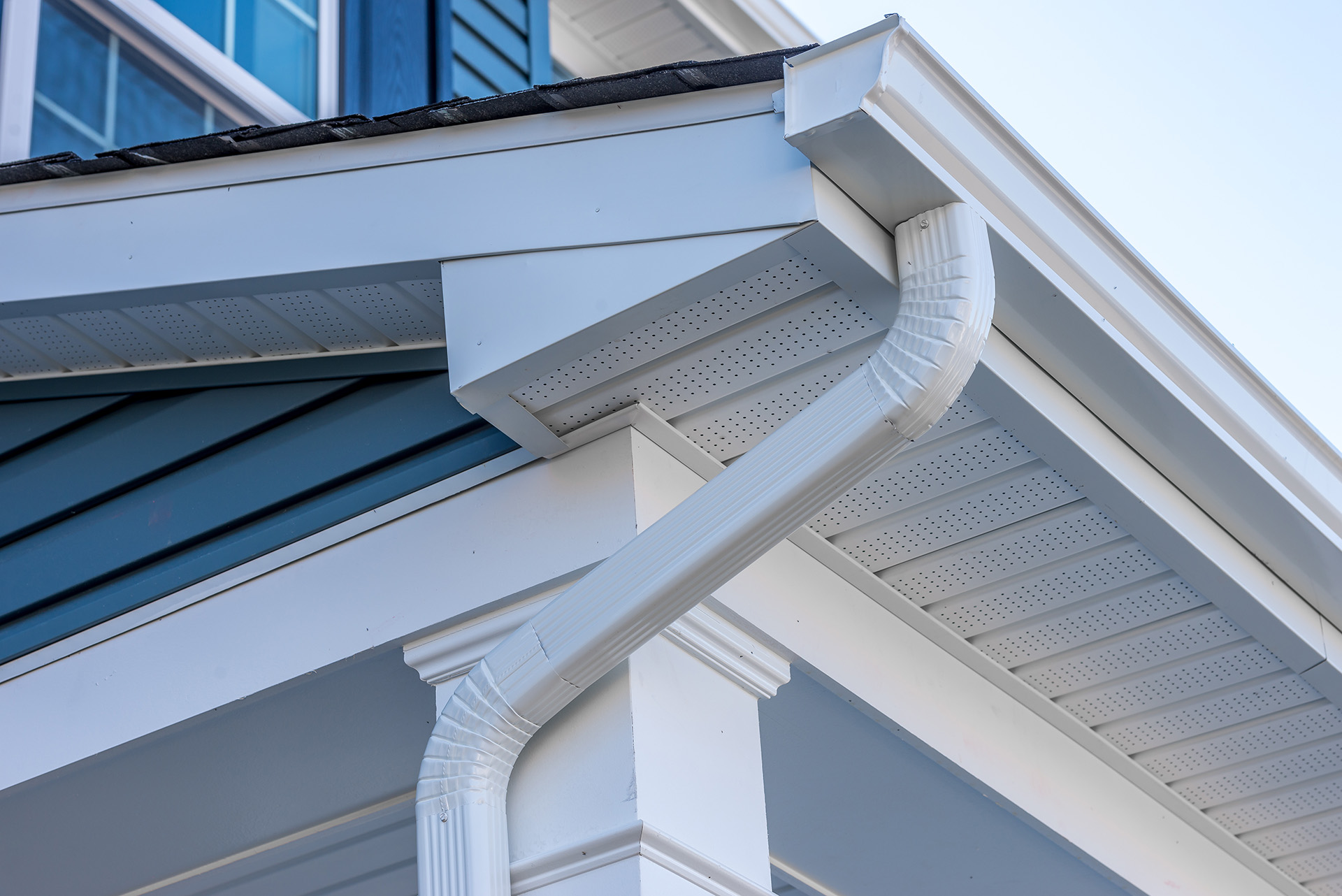 Colonial white gutter guard system, fascia, drip edge, soffit providing ventilation to the attic, with pacific blue vinyl horizontal siding at a luxury American single family home neighborhood