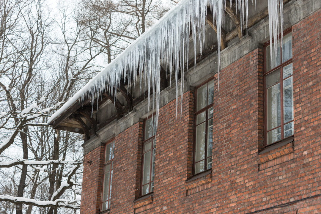 Ice stalactite hanging from the roof with red brick wall. Winter season